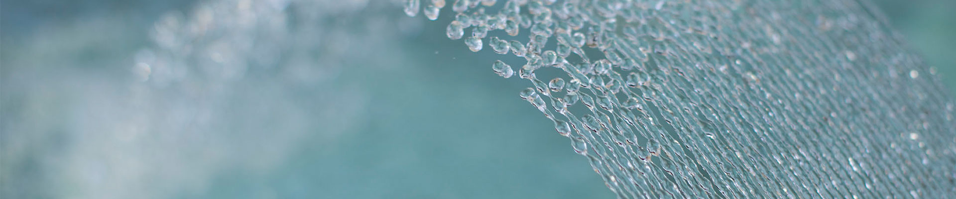 Close-up of water droplets cascading in a clear stream against a blurred greenish background, creating a refreshing and serene visual effect.