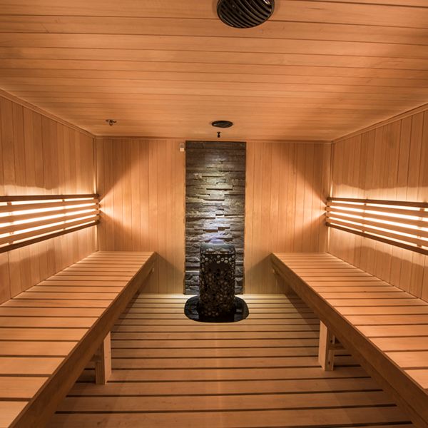 A wooden sauna room with benches and a central stone heater. Soft lighting creates a warm and inviting atmosphere for relaxation.