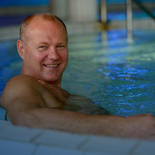 A person relaxes in an indoor pool, smiling with water surrounding them, creating a calm and serene atmosphere under blue lighting.