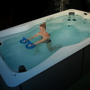 A person exercises in a swim spa using aquatic dumbbells, surrounded by dark surroundings, showcasing commitment to fitness and water-based workouts.