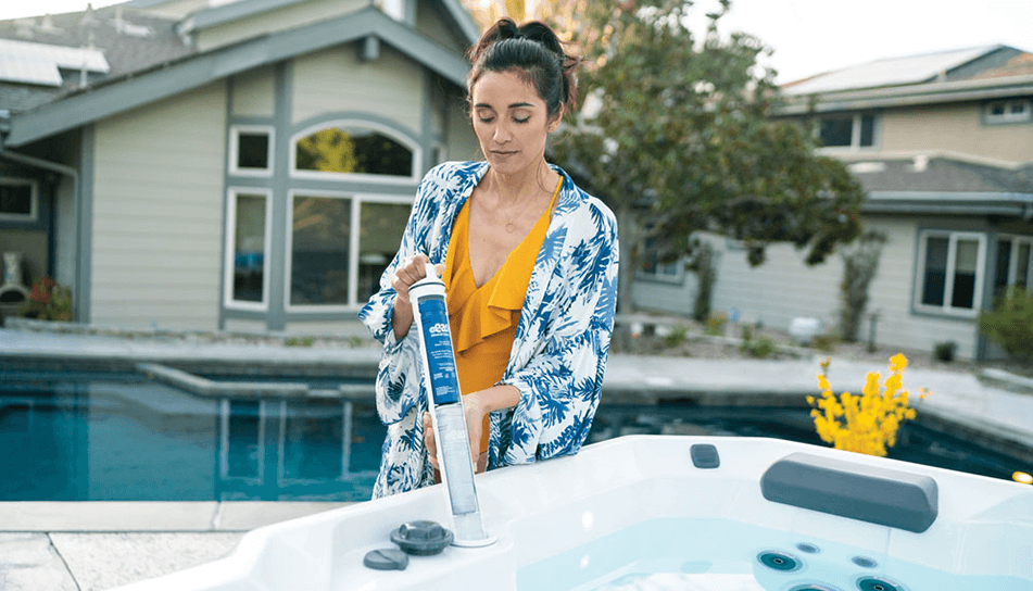 A person in a blue floral robe adjusts a hot tub by a pool in a modern backyard setting.