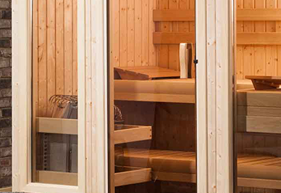 A wooden sauna interior with a warm glow features wooden benches and a small heater, viewed through a glass door.