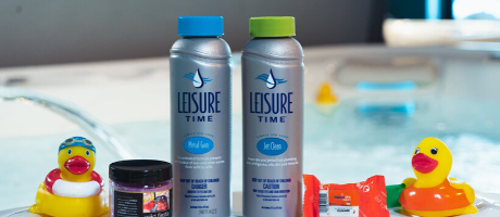 Two bottles of Leisure Time spa care products are by a hot tub, surrounded by rubber ducks and small containers.